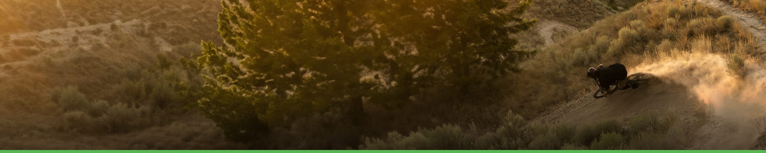 Cycliste en VTT dévalant une pente poussiéreuse au coucher du soleil, entouré de nature sauvage. Logo HopeHOPE